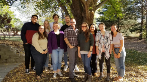 Eleven people pose for a photo in front of a tree