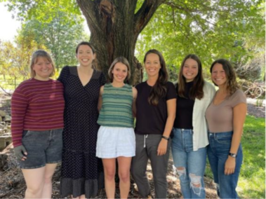 Six people pose for a photo in front of a tree