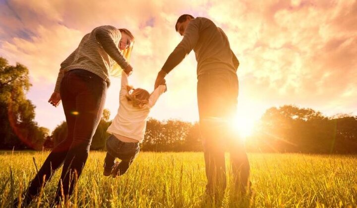 Couple playfully swings young child by arms as sun sets.